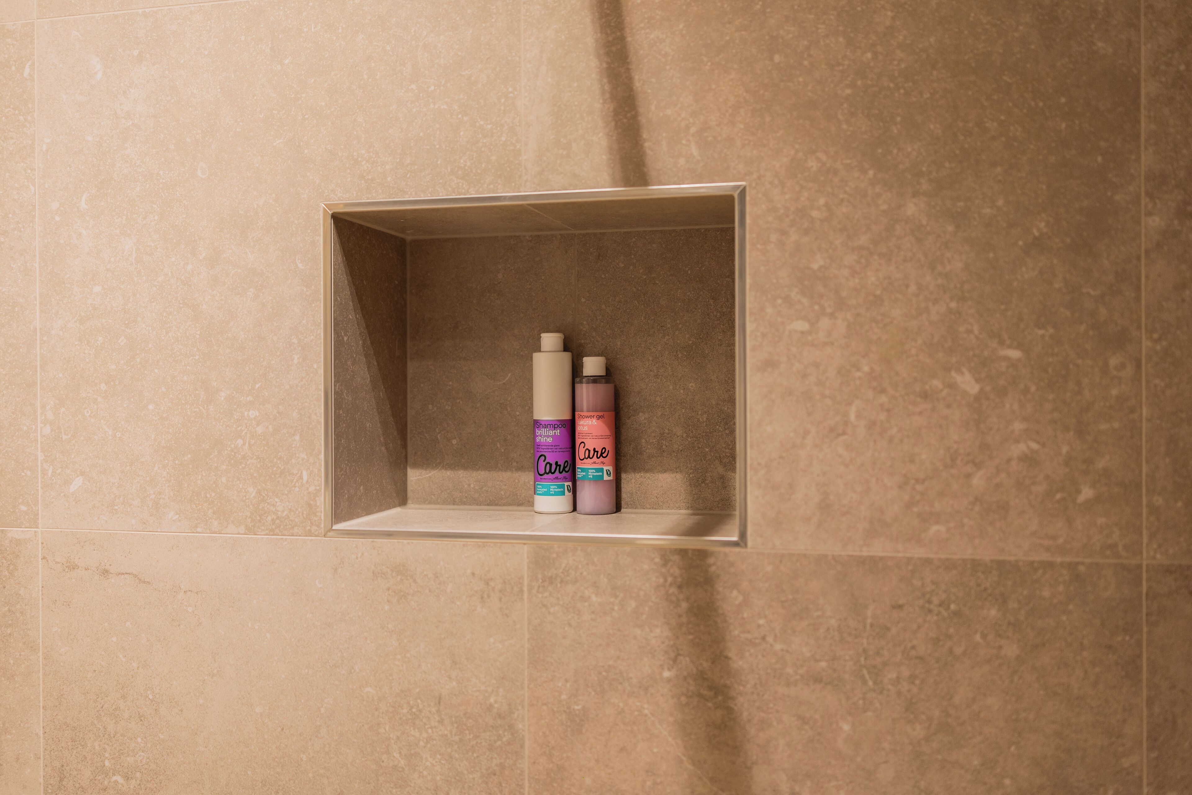 Een badkamer met een beige betegelde muur en een plank met twee flessen shampoo en conditioner.