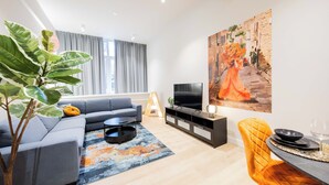 Un salon moderne avec un canapé gris, une table basse noire et un téléviseur à écran plat posé sur un meuble noir.