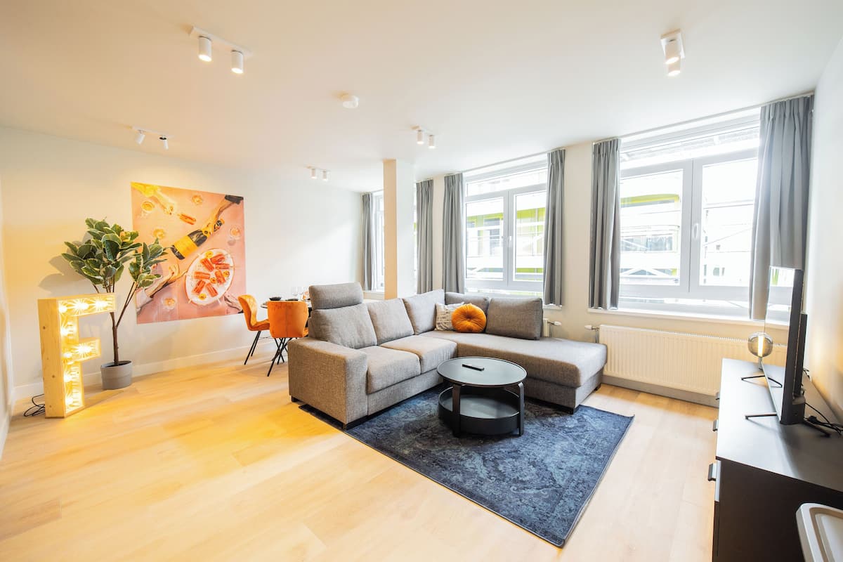 Ein modernes Wohnzimmer mit einem Ecksofa, einem Couchtisch und einem großen Fenster mit Vorhängen.