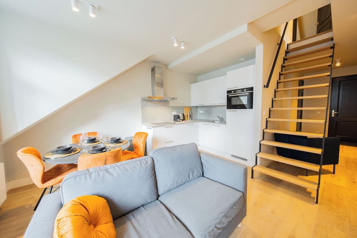 Eine moderne Küche mit weißen Schränken, einem eingebauten Backofen und einer Treppe, die in ein Obergeschoss führt.