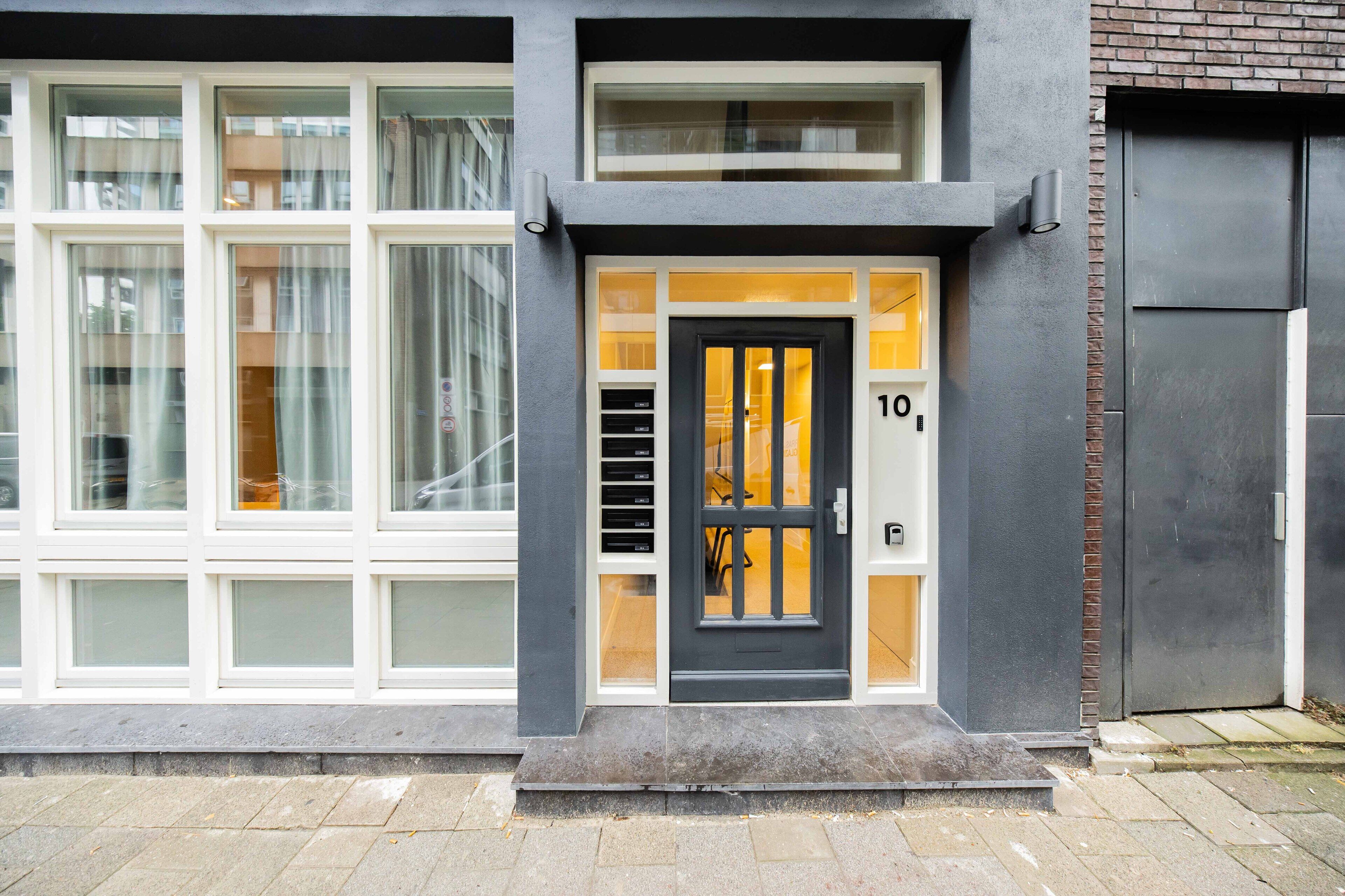 A modern building with a grey facade, a black door with the number 10, and large windows with curtains.