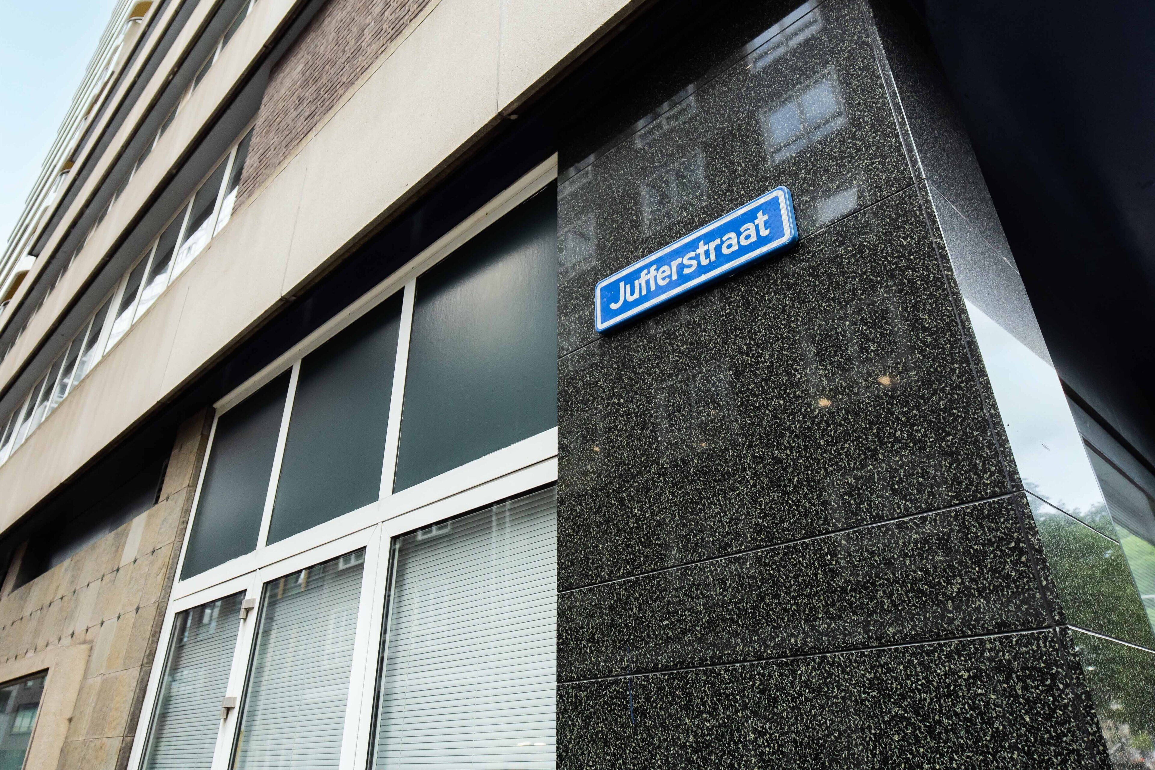 A building facade with a sign reading "Jufferstraat" and a window with a closed shutter.