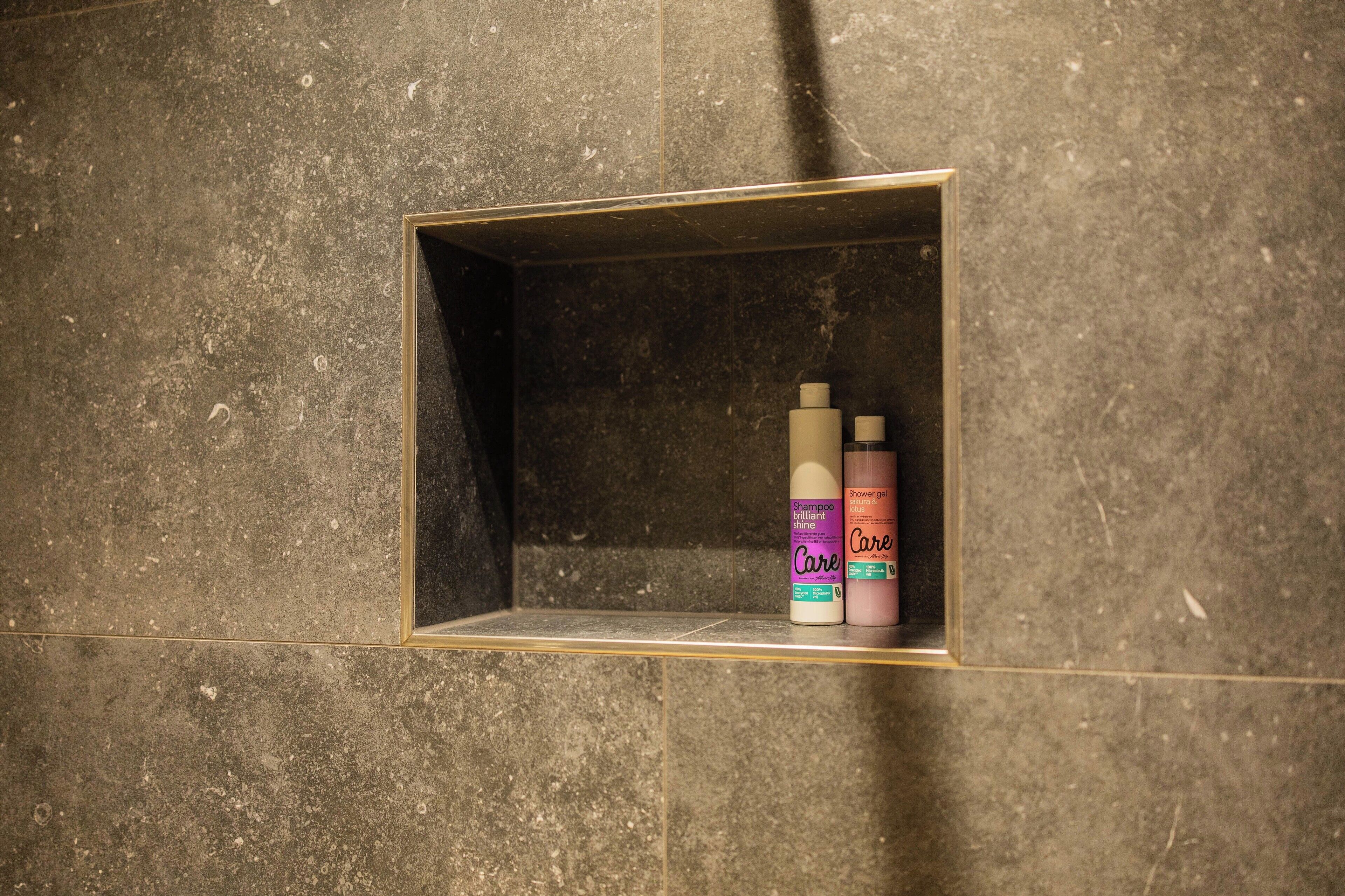 Un bagno con uno scaffale integrato che contiene una bottiglia di shampoo e una di bagnoschiuma.