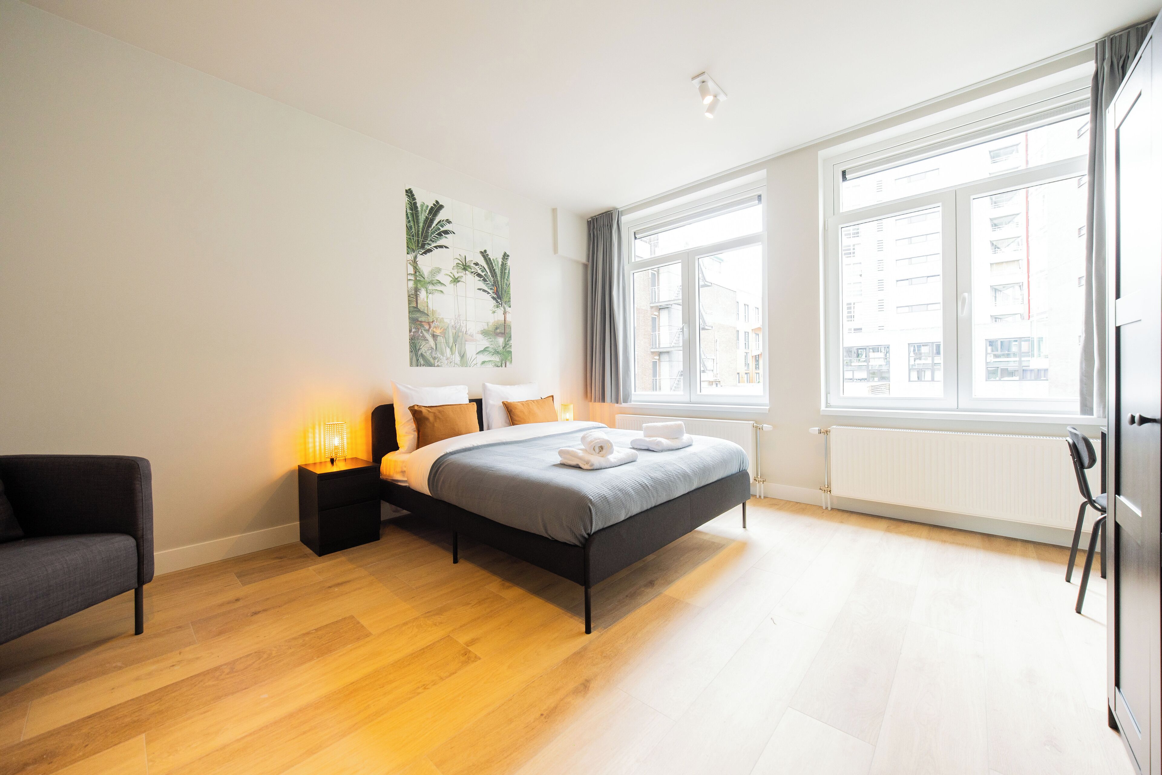 A modern bedroom with a bed, bedside tables, a chair, and large windows.