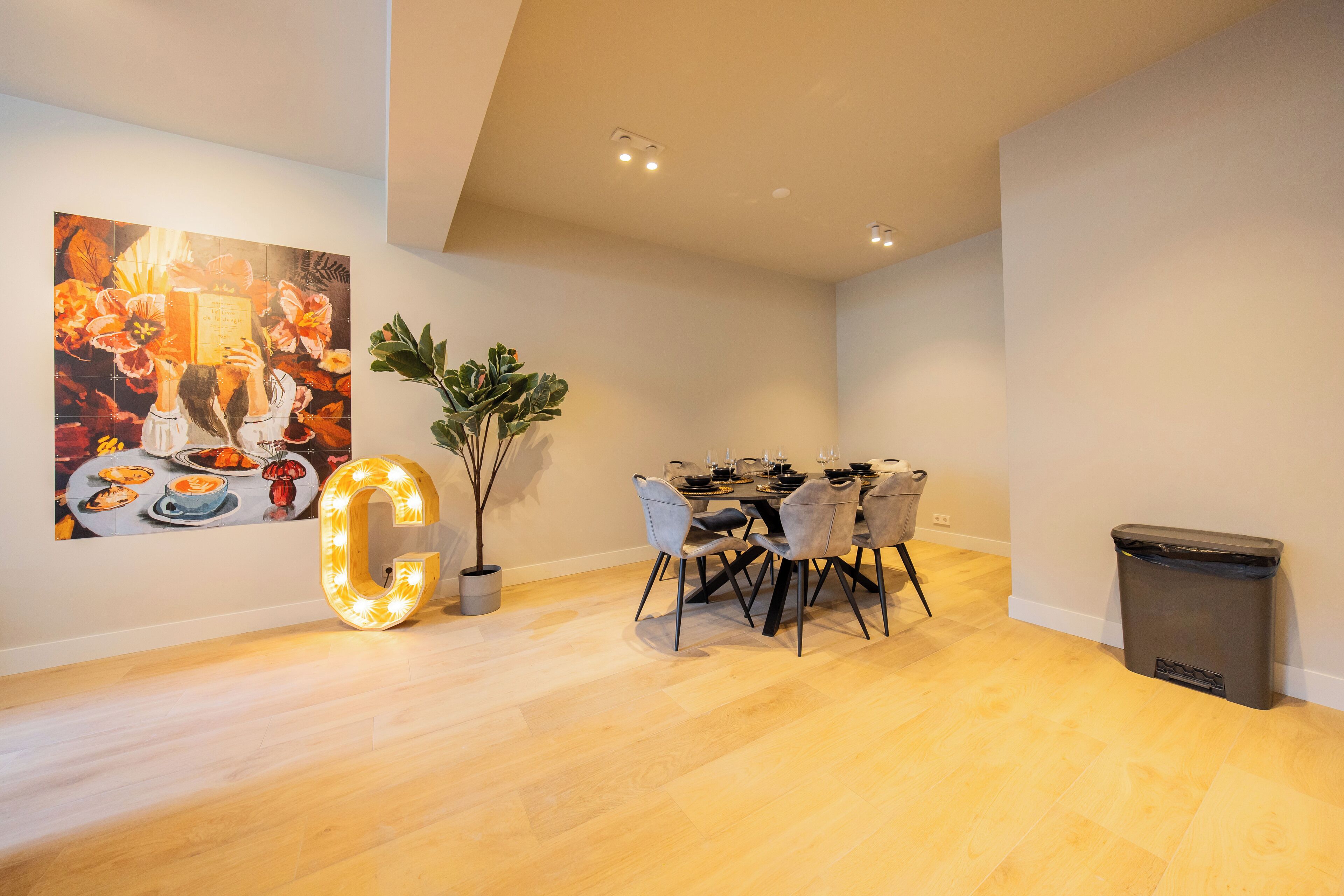A modern dining area with a wooden floor, a table set for four, and a large illuminated 'G' sign.
