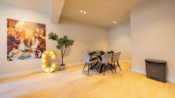 A modern dining area with a wooden floor, a table set for four, and a large illuminated 'G' sign.