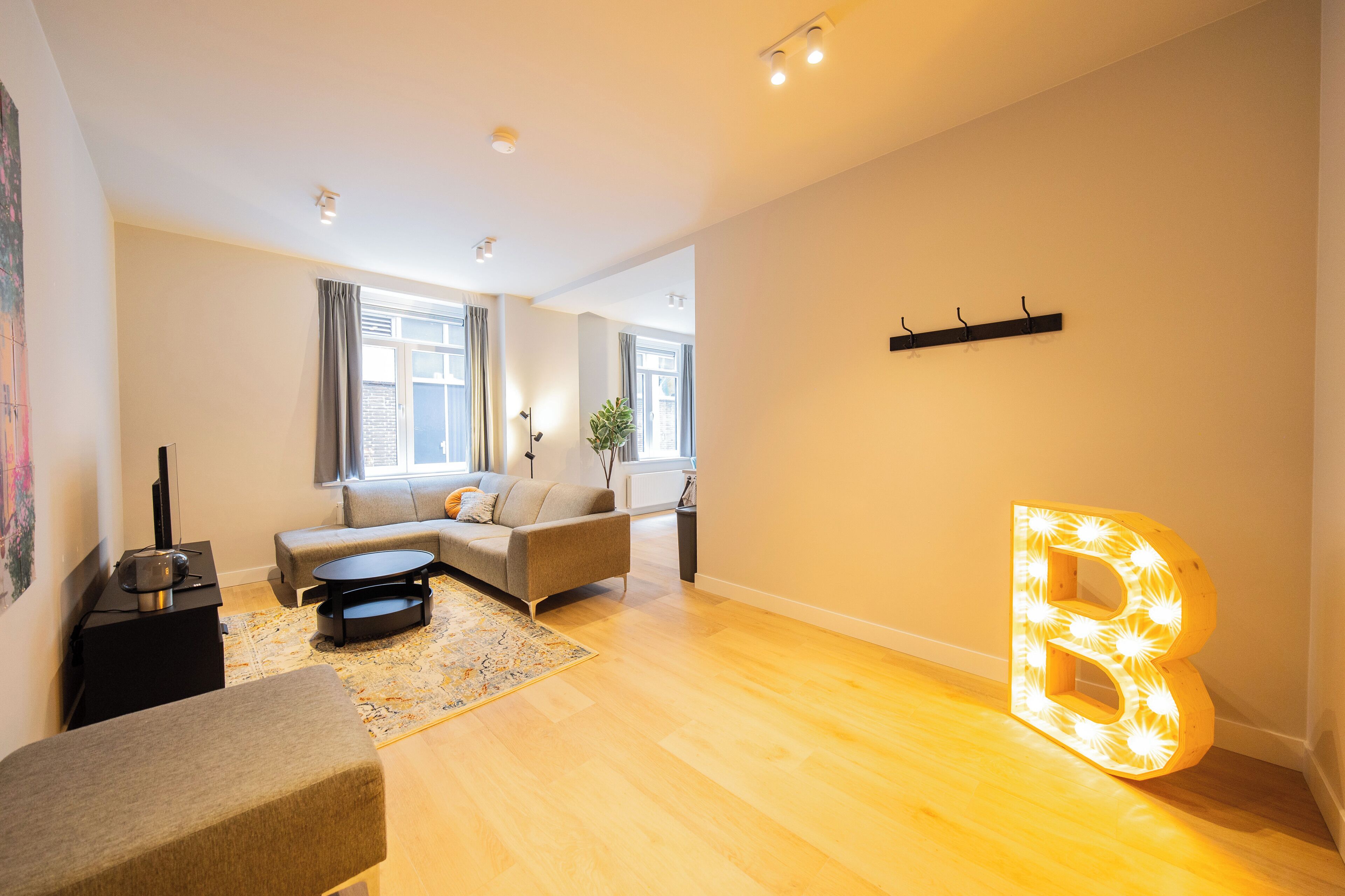 A modern living room with a sofa, a coffee table, and a large illuminated letter 'B'.