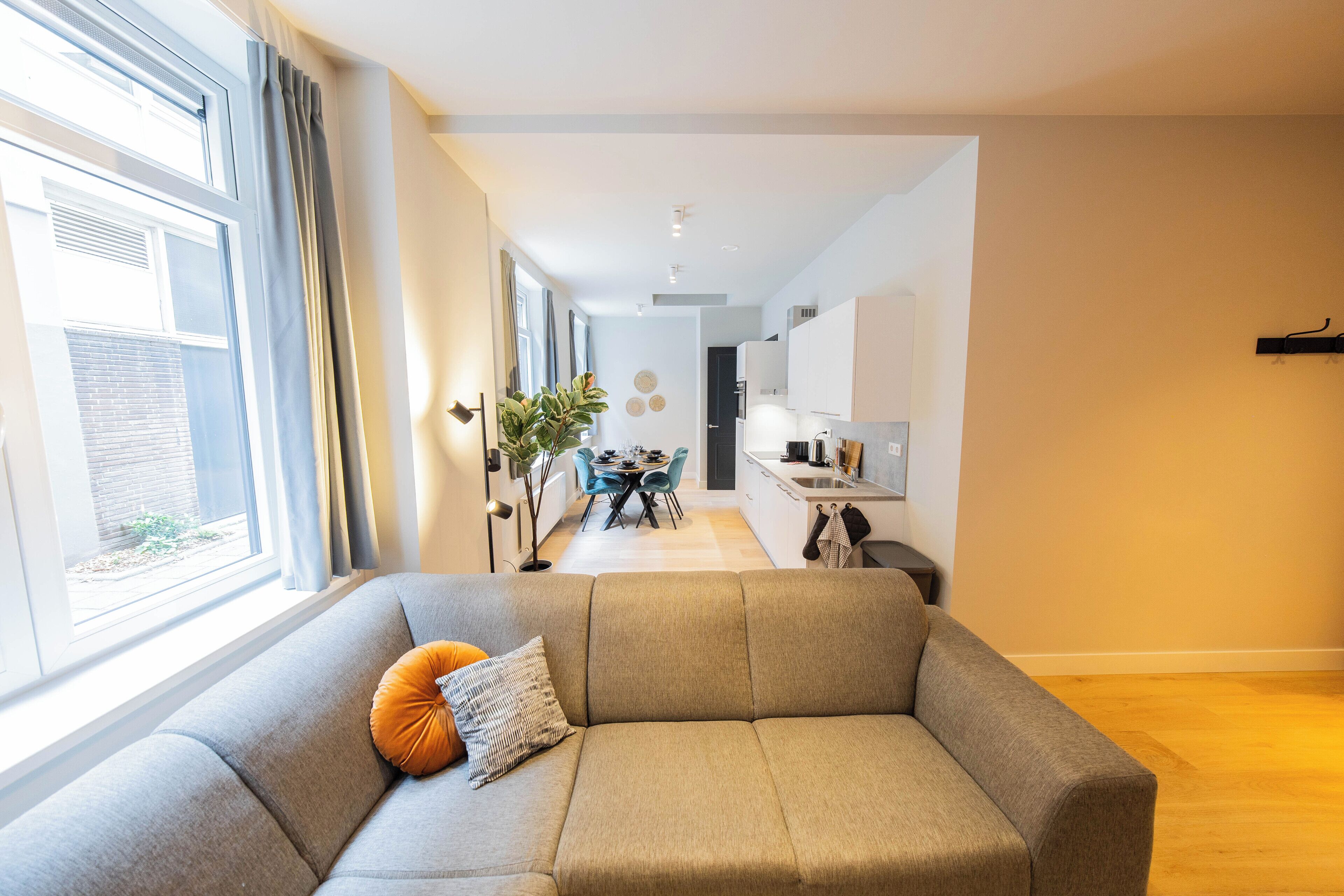 A modern living room with a sofa, a dining area, and a kitchen in the background.