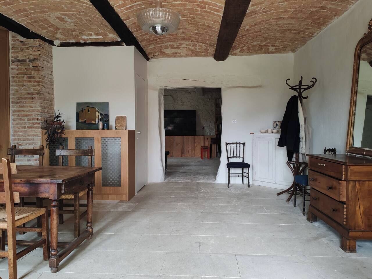 A rustic interior with a wooden dining table, a chair, a wooden cabinet, and a mirror on the right.