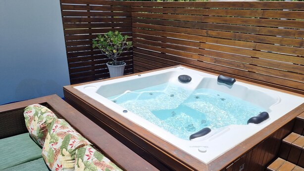 Ein Whirlpool mit Holzterrasse und einer Sitzbank mit floralem Kissen.