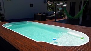 Ein rechteckiger Swimmingpool mit Holzterrasse, umgeben von Gartenmöbeln und einer Hängematte.