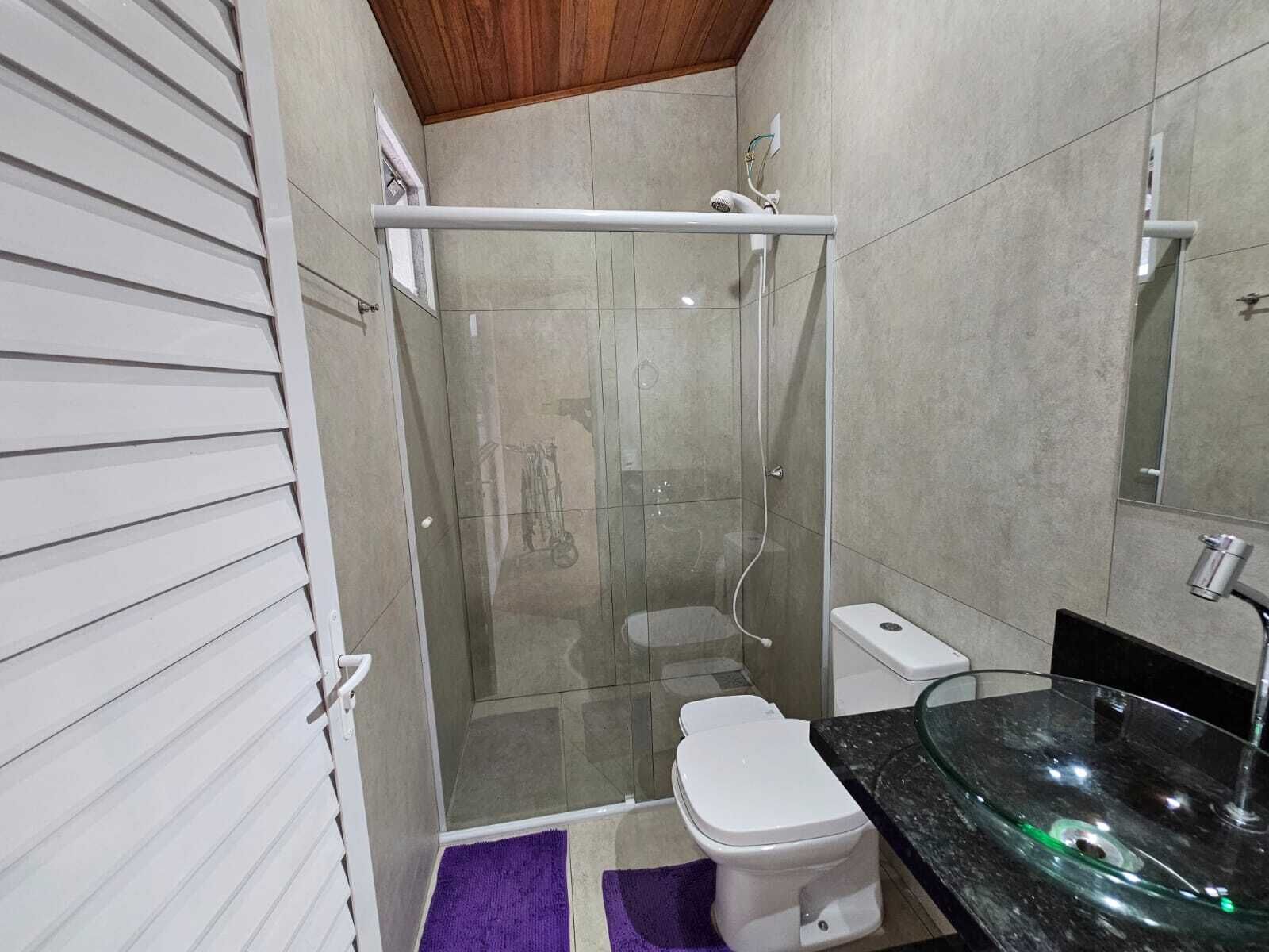 Un baño con cabina de ducha de vidrio, inodoro blanco, lavamanos de vidrio y una alfombra morada.