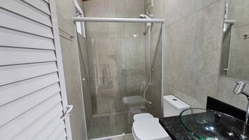 Un baño con cabina de ducha de vidrio, inodoro blanco, lavamanos de vidrio y una alfombra morada.