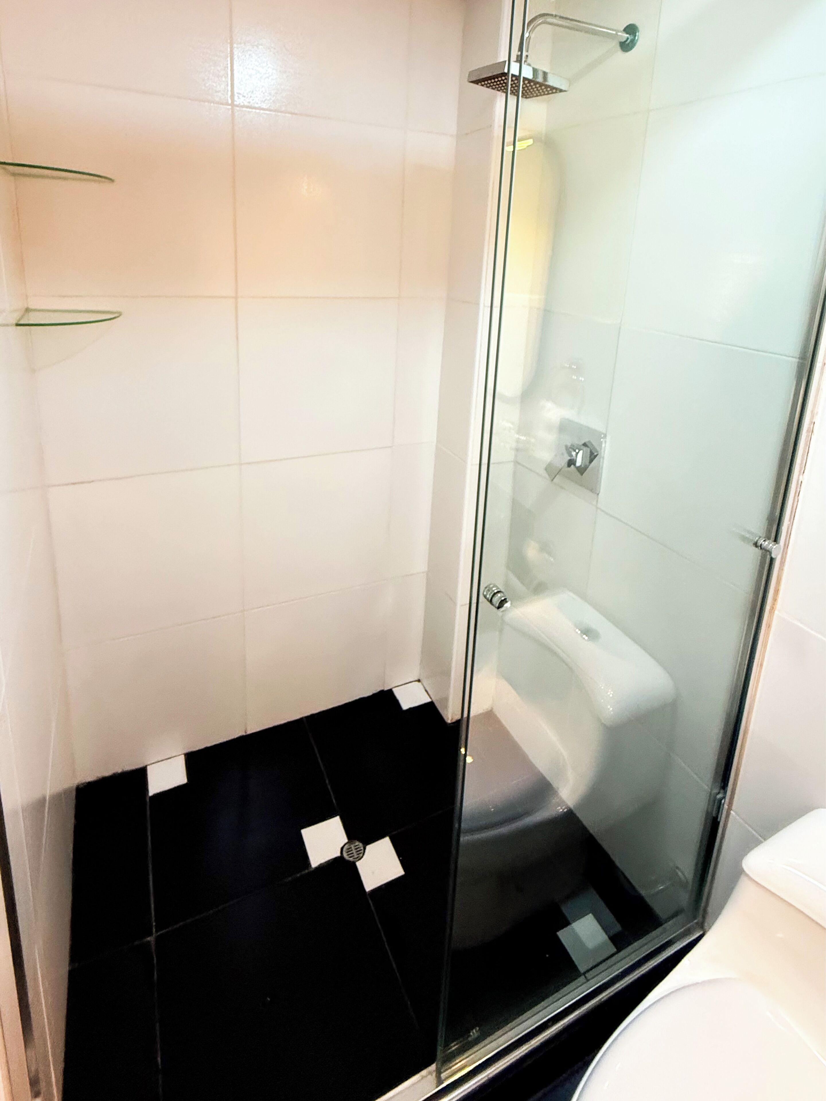 Une salle de bain moderne avec une douche à l’italienne en verre, des toilettes blanches et un sol carrelé de noir.