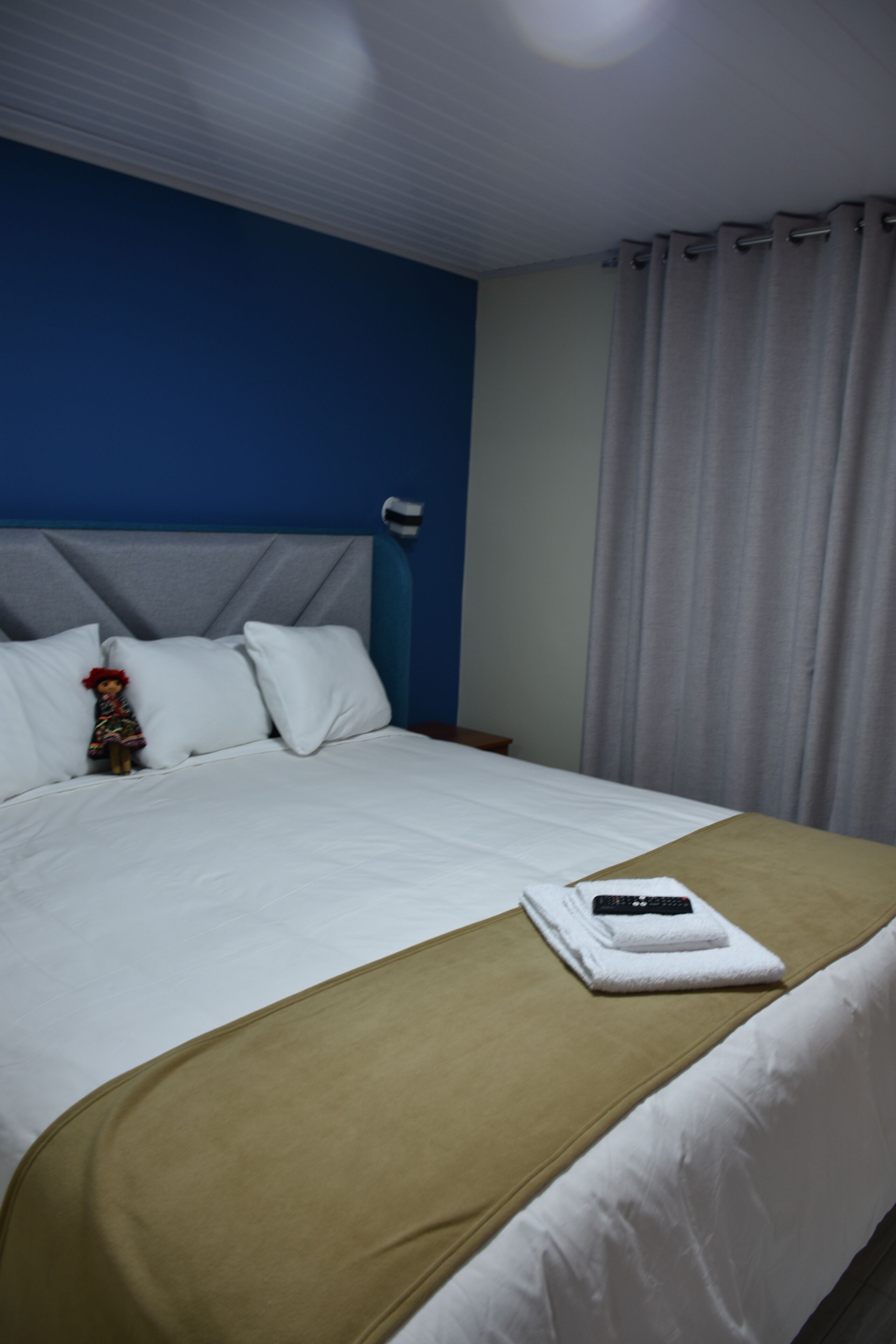 Ein ordentlich bezogenes Bett mit weißen Leinen, einer beige farbenen Tagesdecke und einer Fernbedienung auf einem weißen Handtuch.