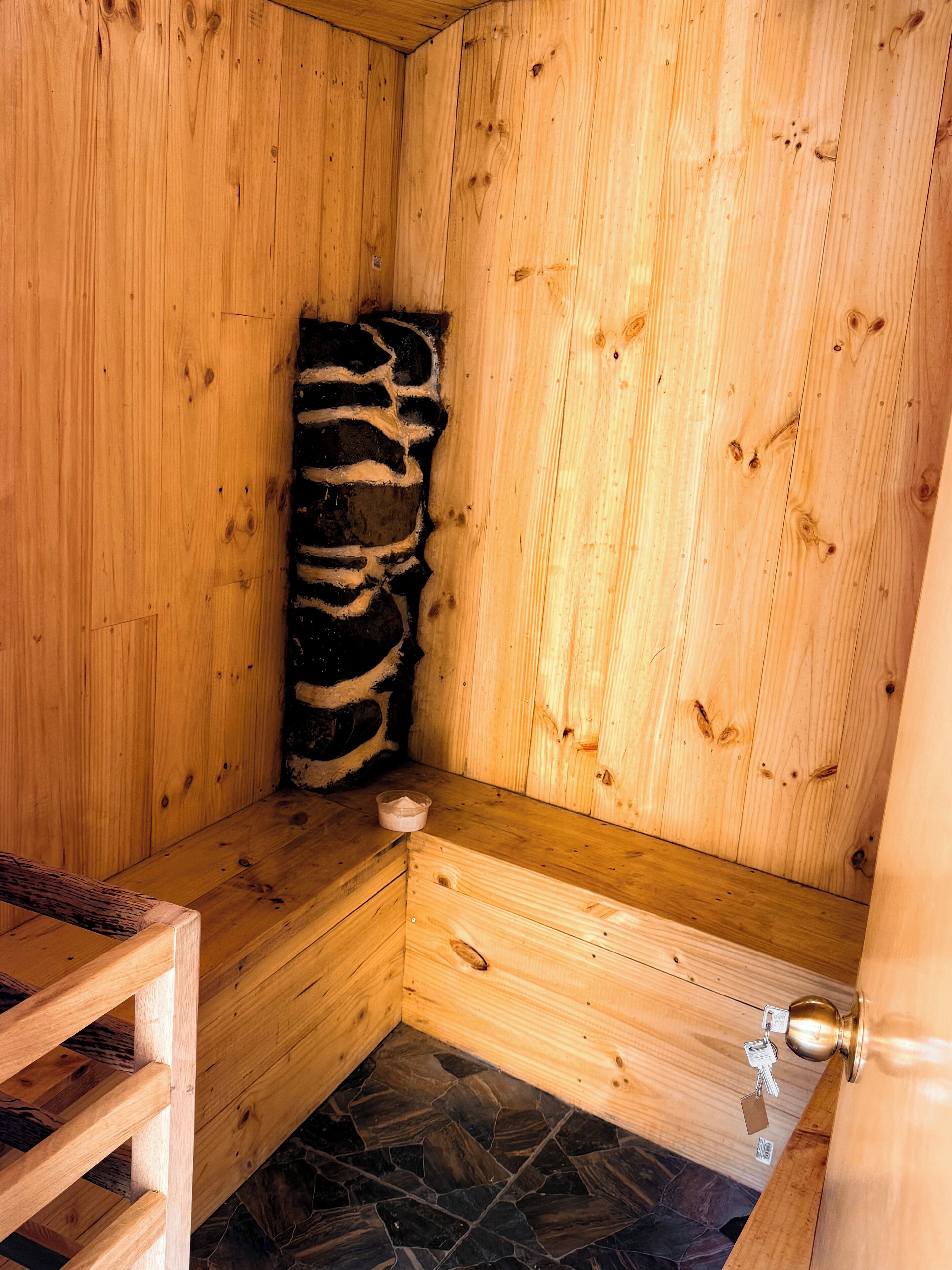 A wooden sauna with a stone floor, a bench, and a small bowl on the bench.