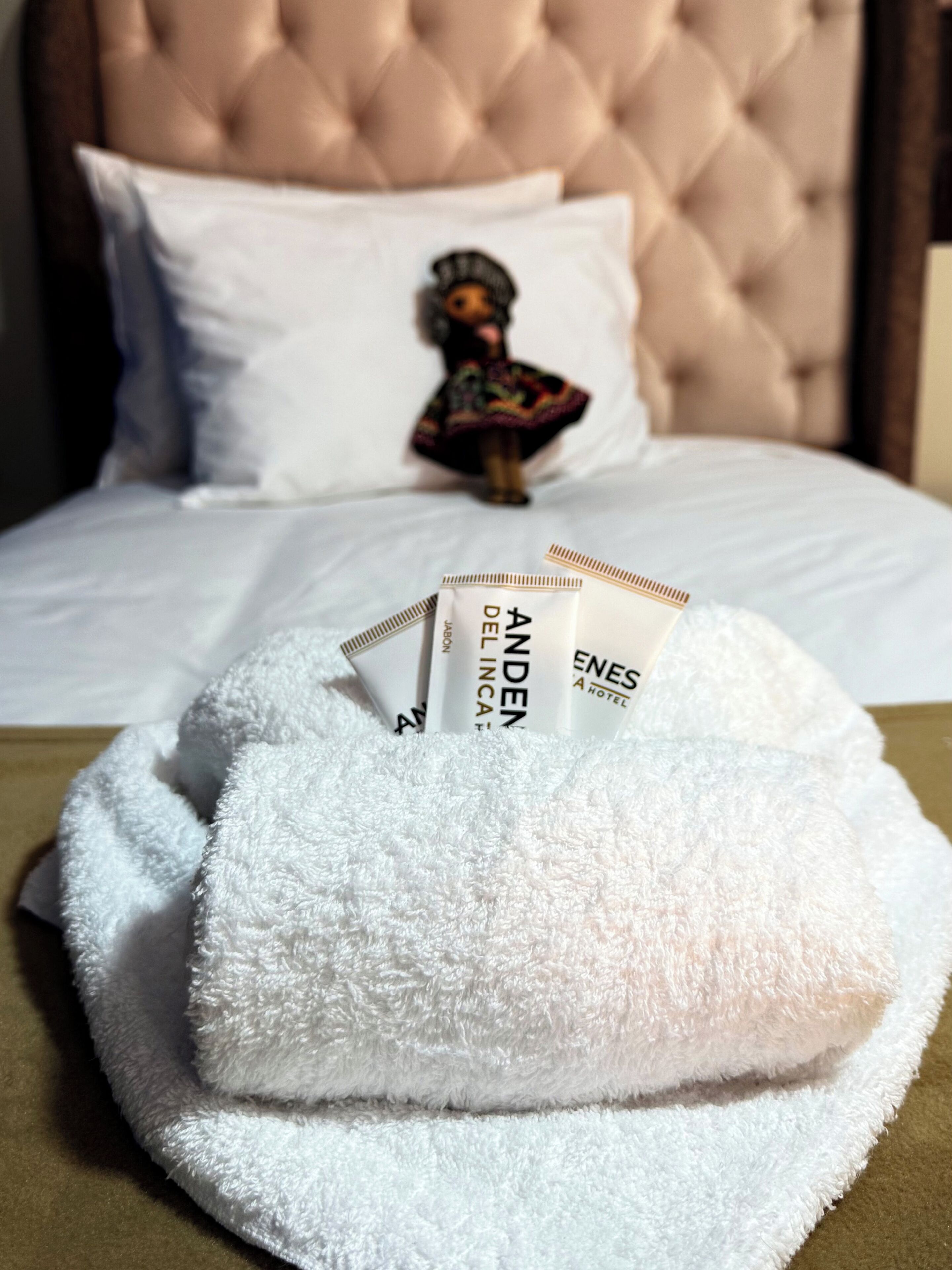 Een net opgemaakt bed met een zacht hoofdbord, een wit kussen en een gevouwen witte handdoek op het bed.
