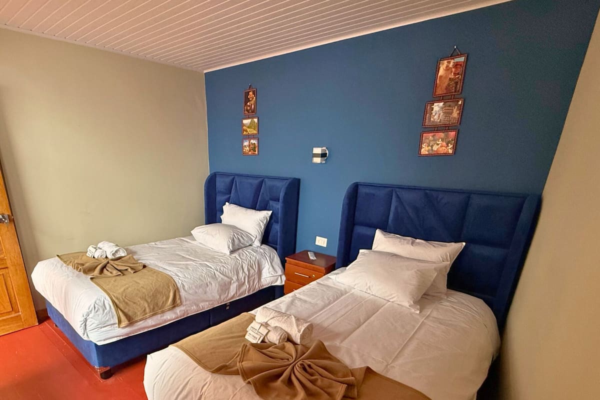 Two double beds with blue headboards and white bedding, a wooden nightstand, and a red carpeted floor.