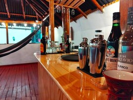 Una zona de bar con mostrador de madera, distintas botellas y vasos.