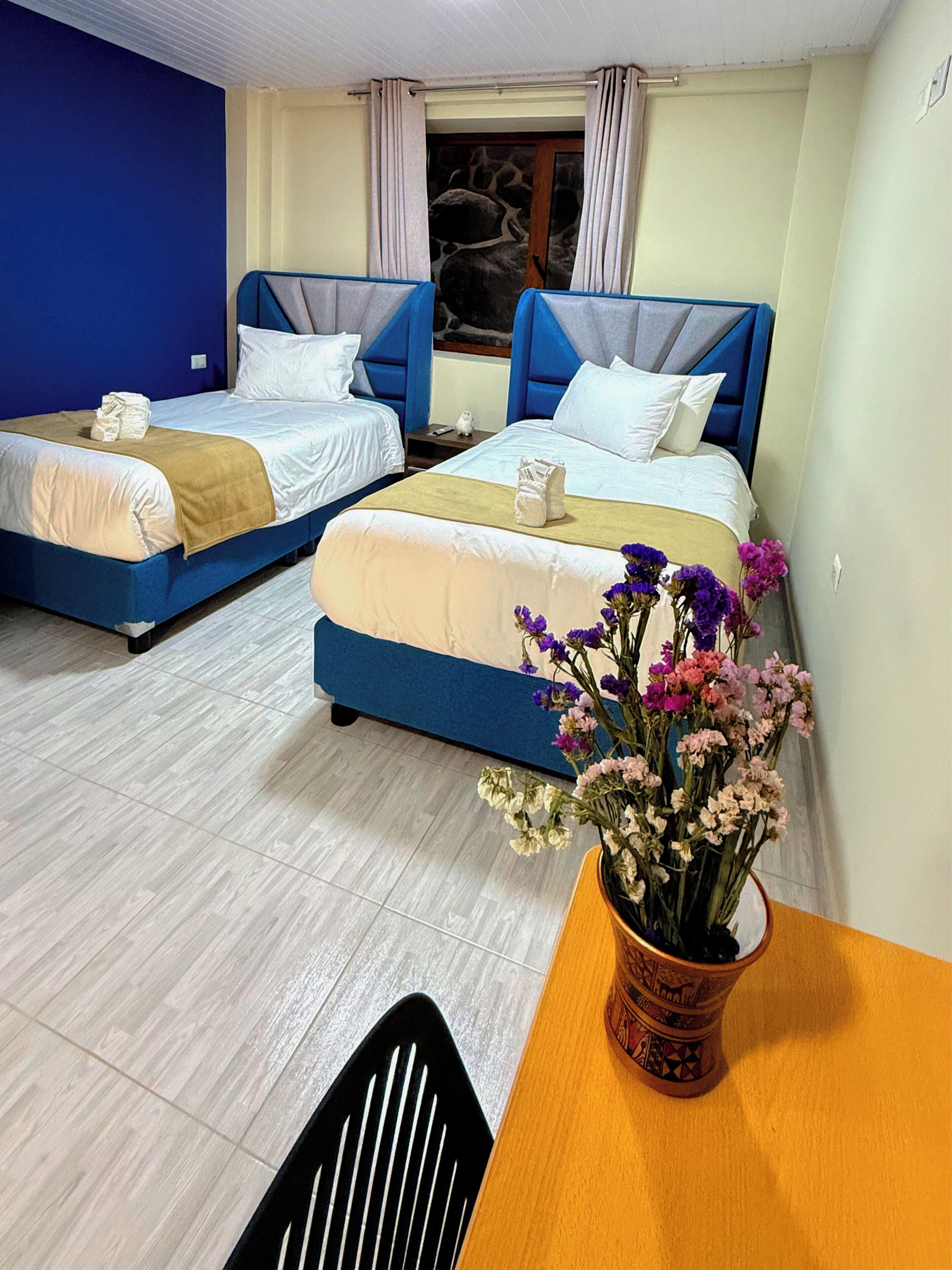 Habitación de hotel con dos camas, una mesa de madera, una silla y un florero con flores.