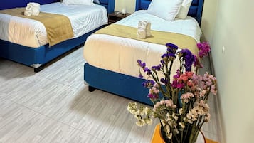 Habitación de hotel con dos camas, una mesa de madera, una silla y un florero con flores.