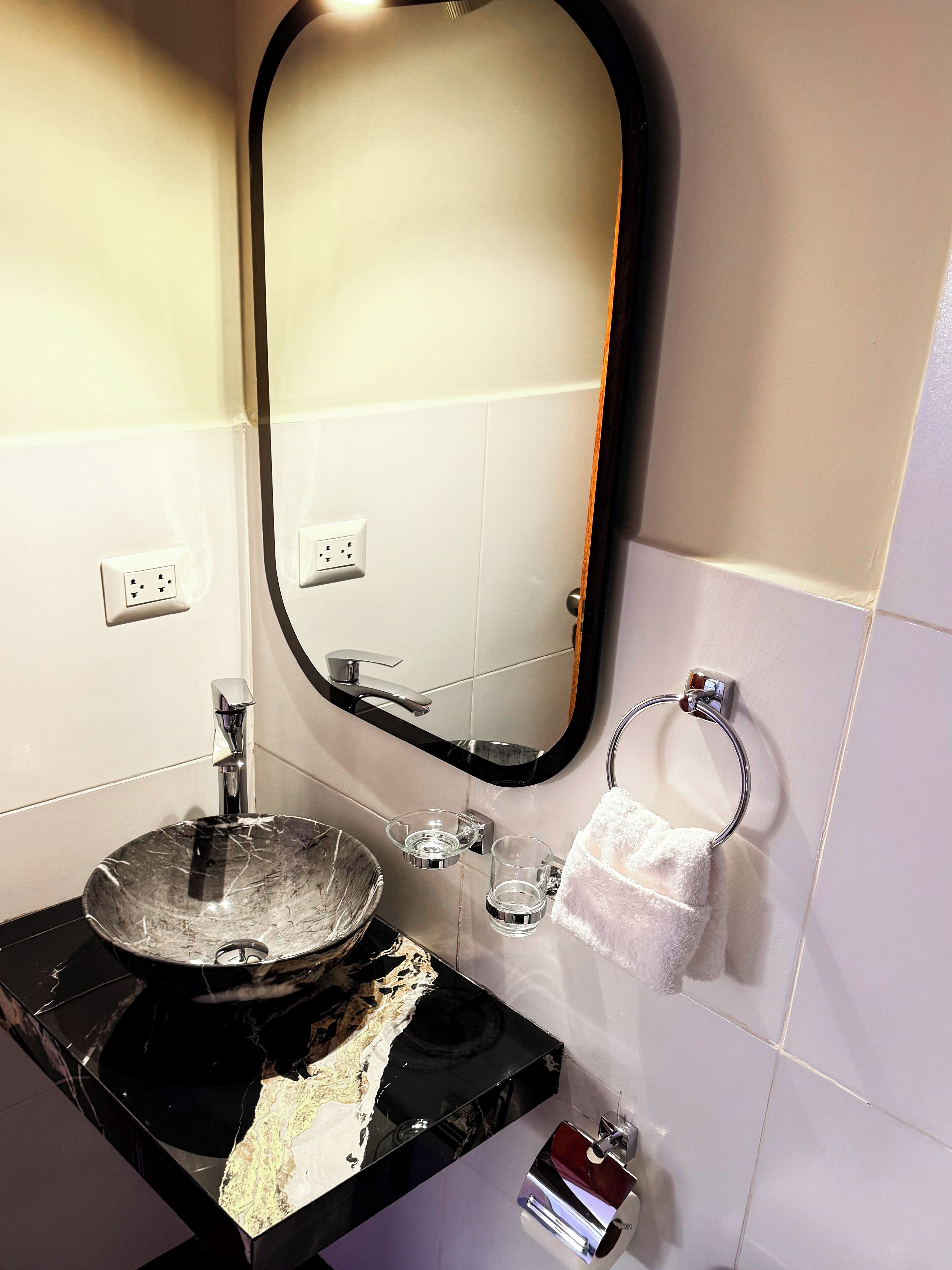 A bathroom with a black marble sink, a mirror, a towel rack, and a glass soap dish.