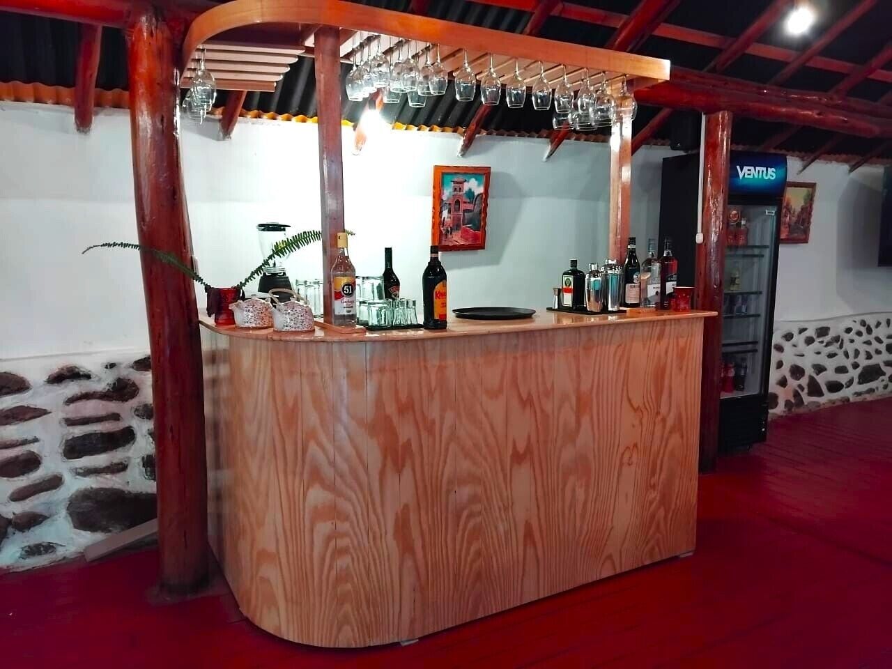 A wooden bar area with bottles and glasses, a stone wall, and a red carpet.