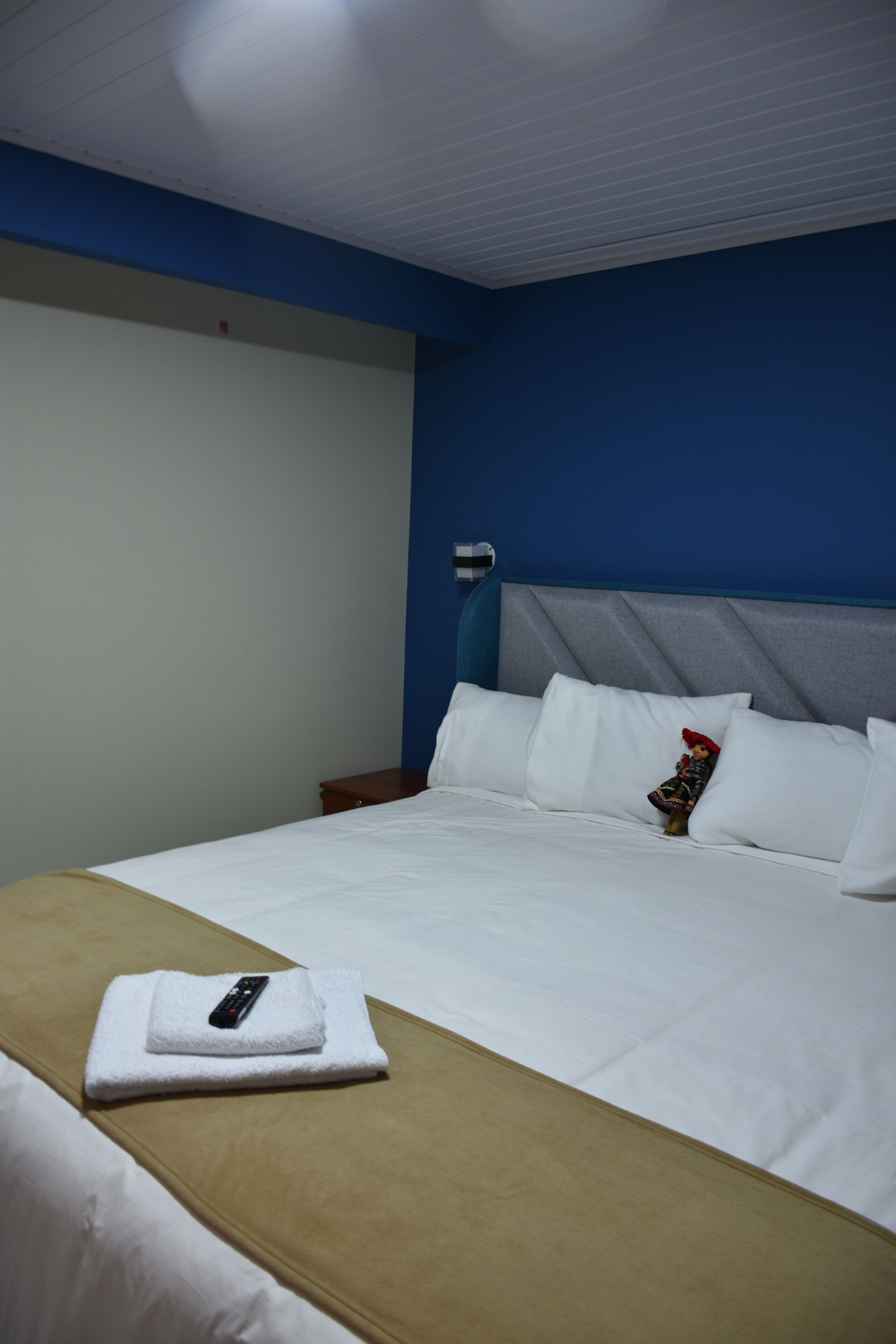 A hotel room with a bed, a nightstand, a remote control, and a decorative item on the bed.
