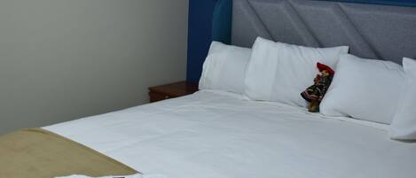 A hotel room with a bed, a nightstand, a remote control, and a decorative item on the bed.