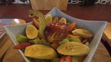 A square bowl filled with sliced fruits and a decorative apple on a wooden table.