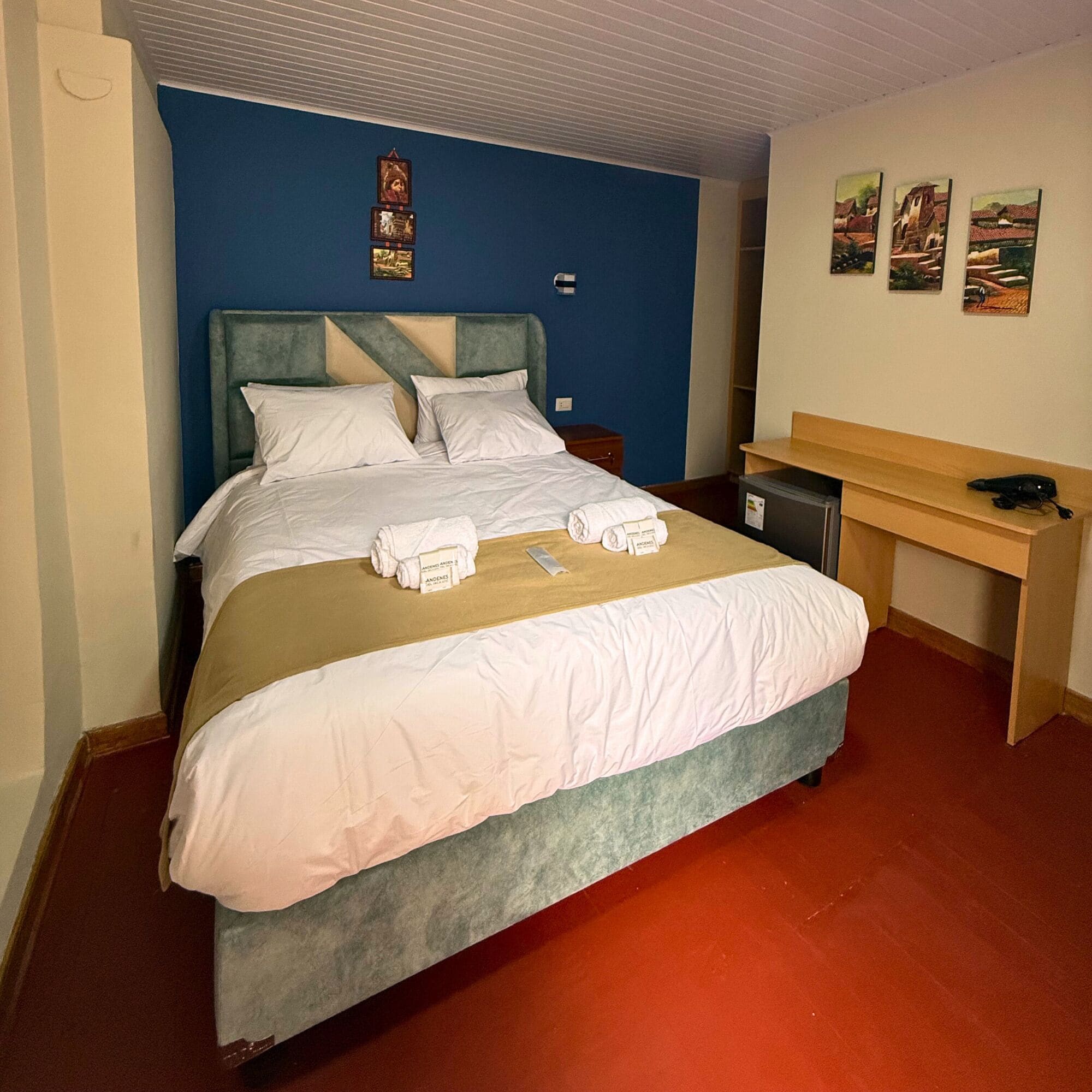 A neatly made bed with white linens, a wooden desk, and a small nightstand.