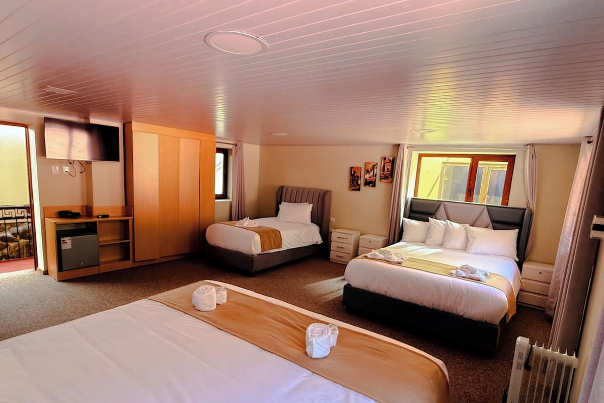 A hotel room with two beds, a desk, a wardrobe, and a radiator.
