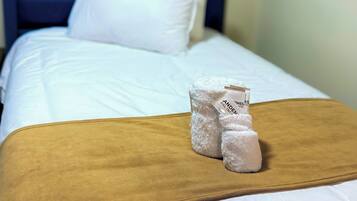 Una habitación de hotel con una cama, ropa de cama blanca, un cabecero azul y una manta marrón.