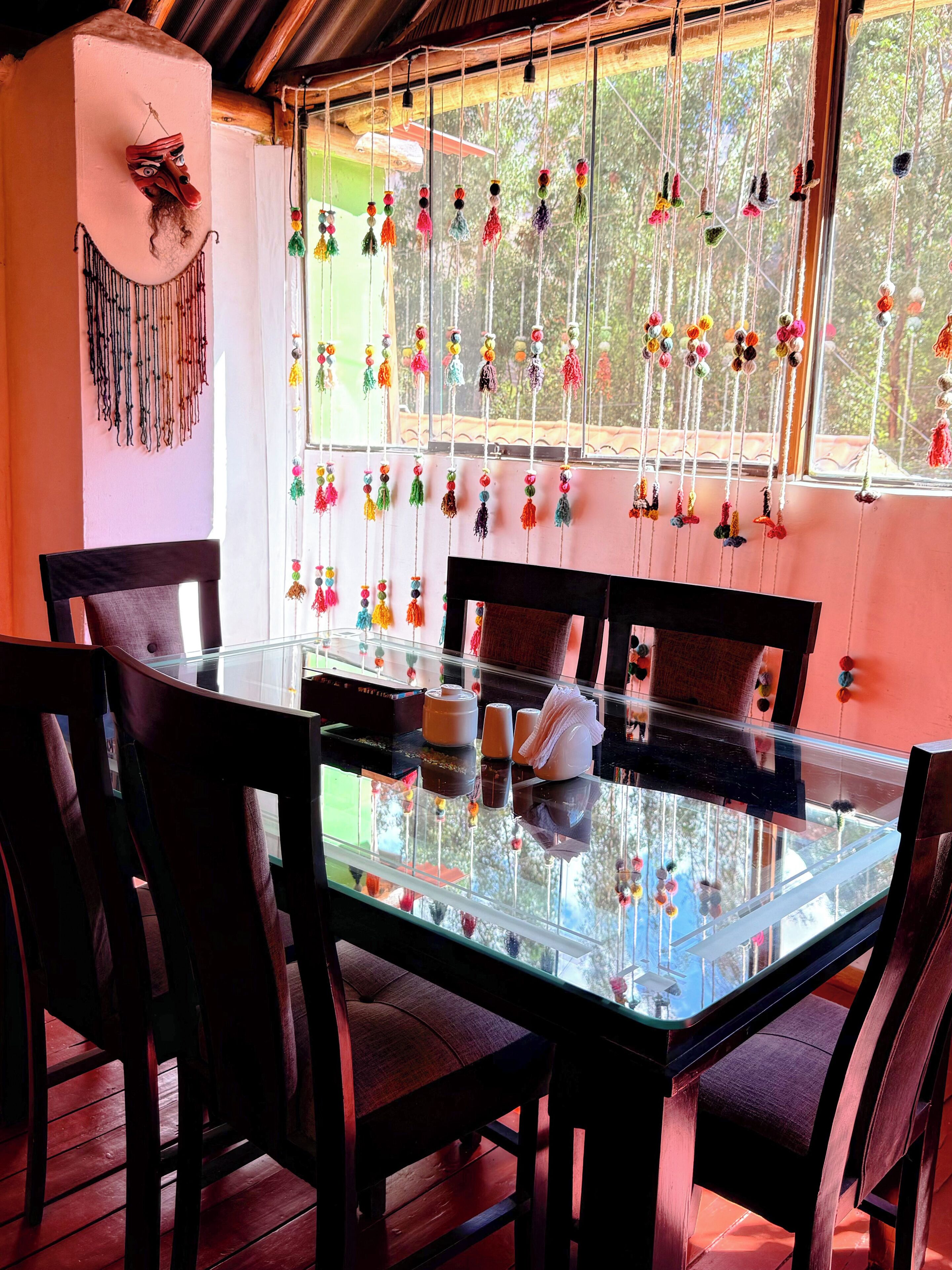 A glass-top dining table with chairs, a decorative mask on the wall, and colorful hanging ornaments.