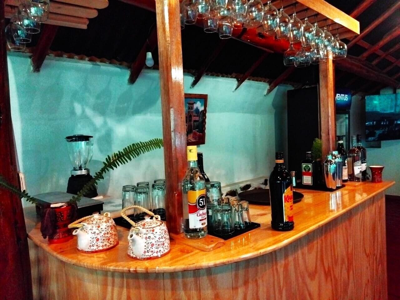 Un espace bar avec un comptoir en bois, diverses bouteilles, des verres et un mixeur.