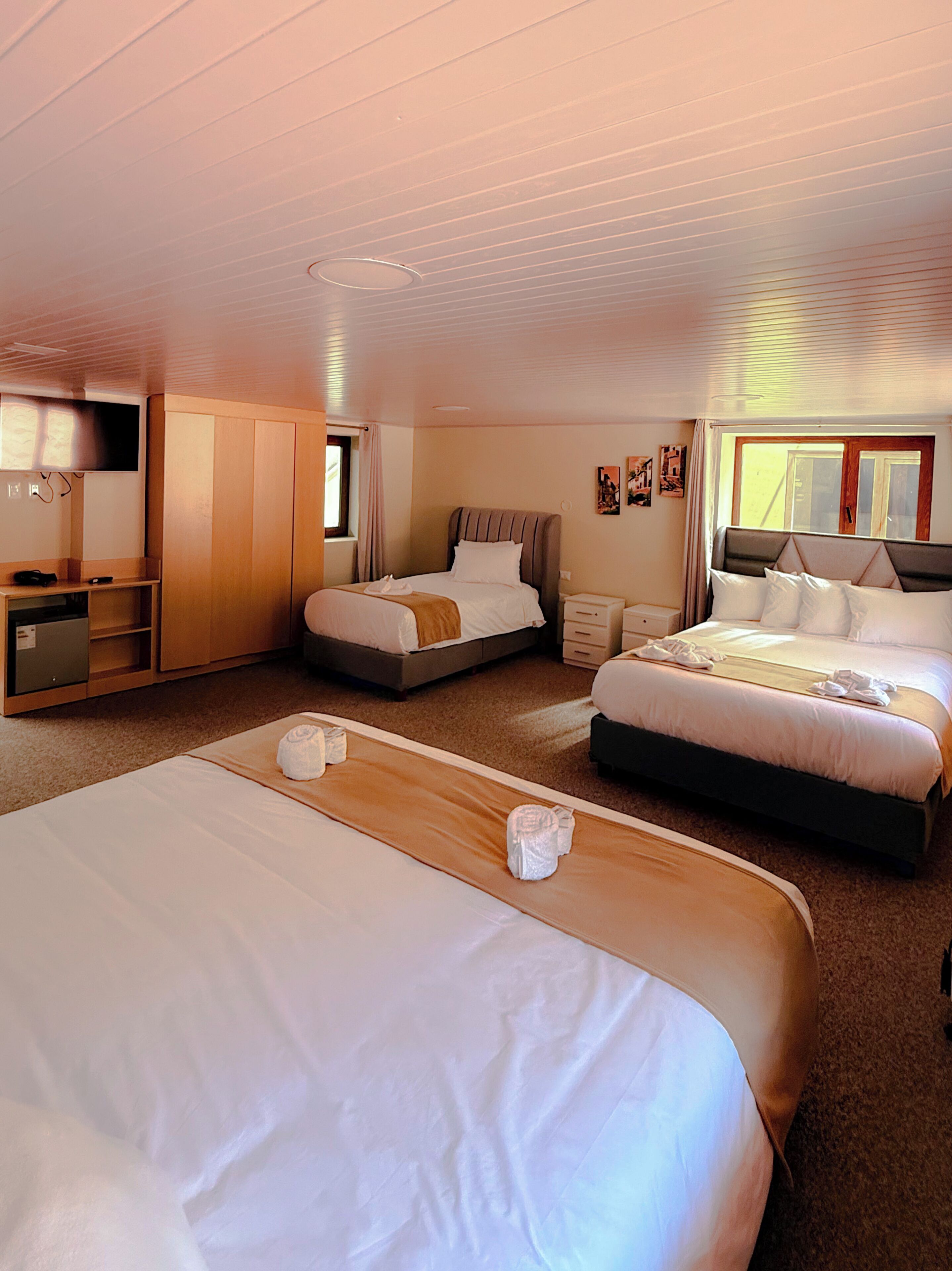 Habitación de hotel con tres camas, un escritorio, un televisor y una ventana.