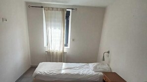 A small, clean room with two single beds, a window with curtains, a bedside table, and a wall-mounted light fixture. - Presqu'île de Chooz (Chooz)