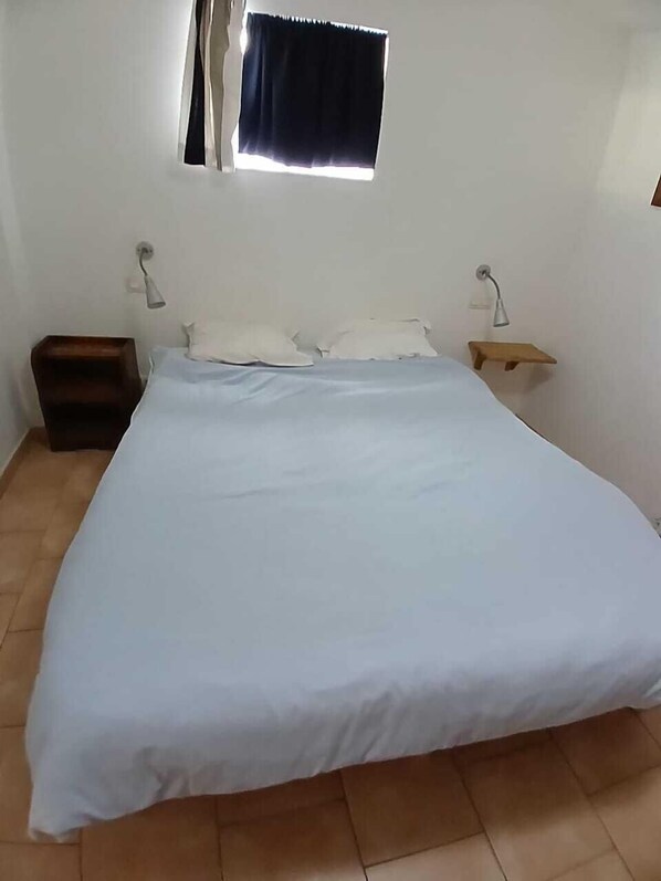 A bedroom with a large bed, two bedside tables, a small wooden bench, and a window with curtains.