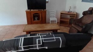 A living room with a black sofa, a wooden TV stand, a white chair, and a small table. - Presqu'île de Chooz (Chooz)