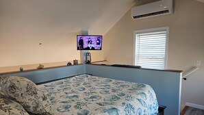 Een slaapkamer met een bed, een aan de muur bevestigde televisie, een raam met zonwering en een airconditioning.
