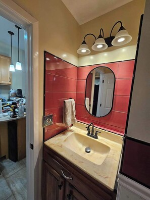 Un baño con lavamanos, espejo y azulejos rojos.