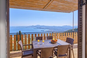 A balcony with wicker furniture, two glasses of orange juice, and a fruit basket. - Christine's Seaview by Corfuescapes (Corfu)