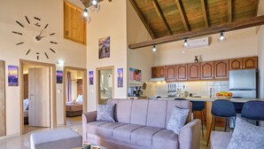 Un saló modern amb un sofà, una taula de centre i una zona de cuina amb armaris de fusta i un frigorífic.