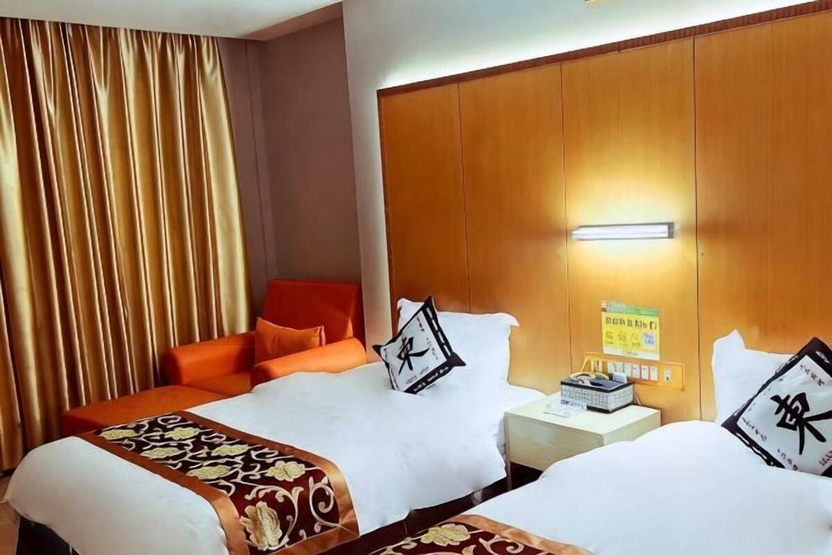 A hotel room with two beds, a wooden headboard, a nightstand, and a curtain.