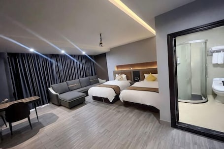 A modern hotel room with a sofa, two beds, a desk, and a shower area.. Hotels in Werner