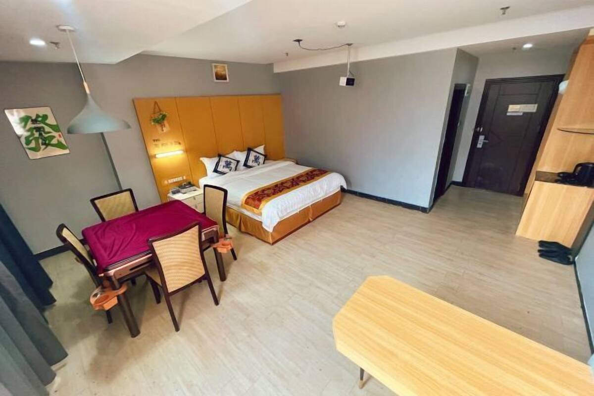 A hotel room with a bed, bedside table, chair, desk, and a bench.