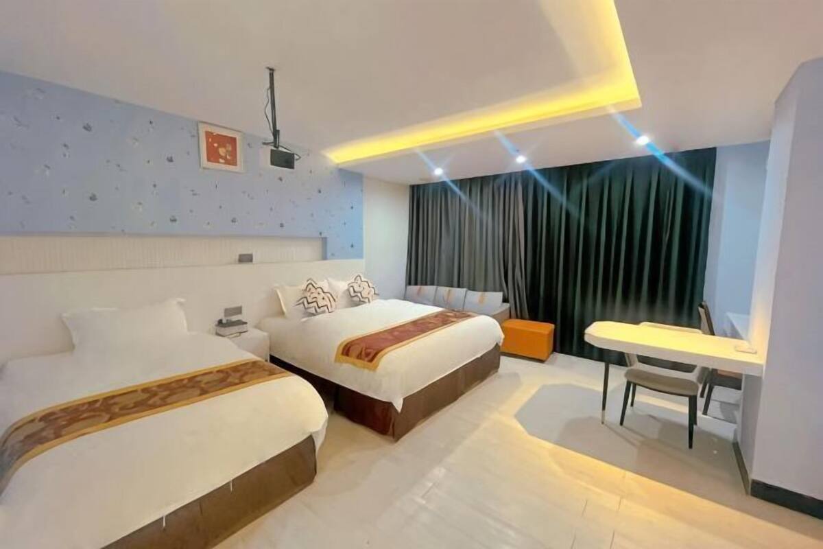 A hotel room with two beds, a desk, a chair, a TV, and a window with curtains.