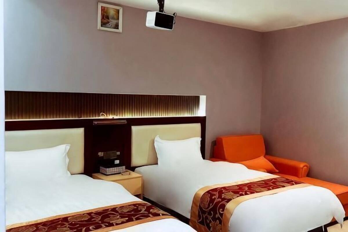 A hotel room with two beds, a nightstand, a television, and a red chair.