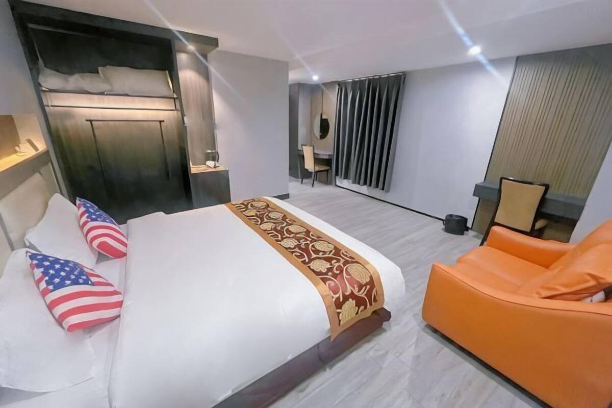 A hotel room with a bed, an orange chair, a desk, and a mirror.