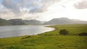A panoramic view of a coastal landscape with a body of water, grassy fields, and distant mountains under a cloudy sky. - Sleep 6 Cottage -petsok, Selfcheck-in, Freeparking (Ardara)